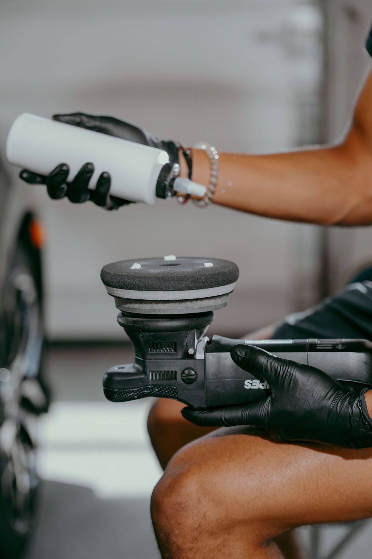 Person applying product to a car polishing machine, wearing black gloves.