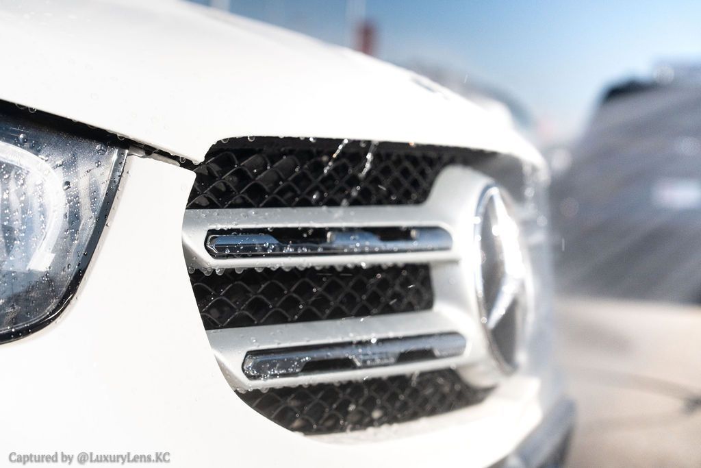 Close-up of a white Mercedes-Benz grille with the company logo, partially covered in snow.