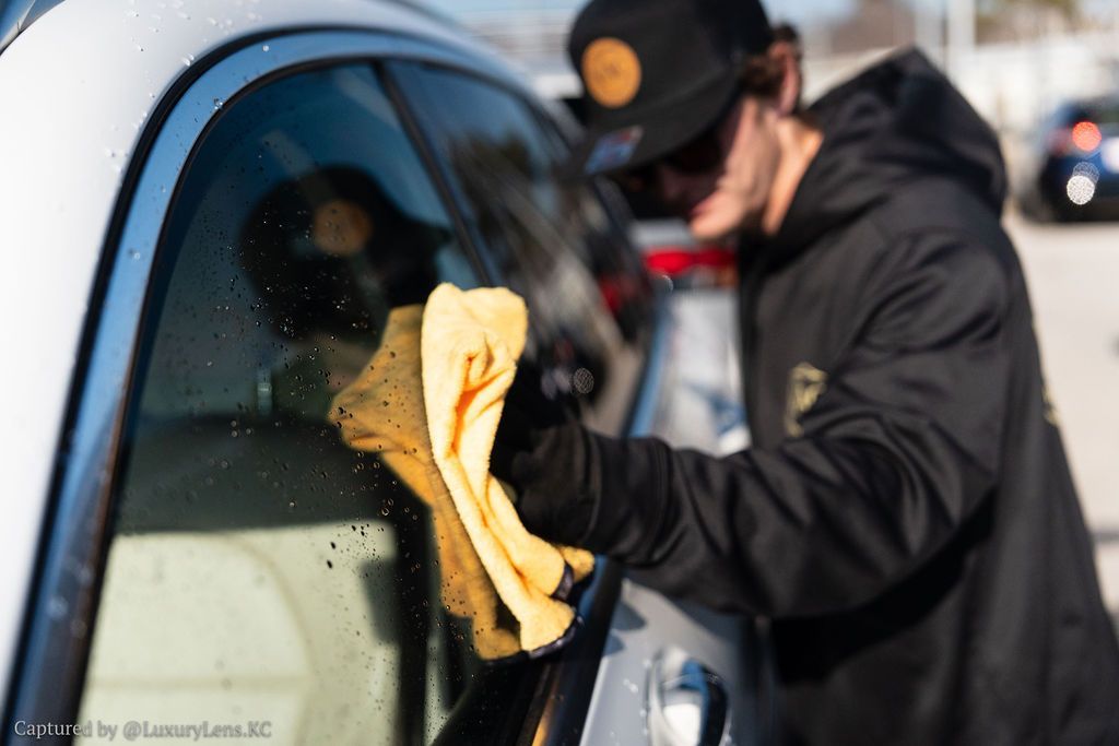 Person cleaning a car window with a yellow cloth, outdoors.
