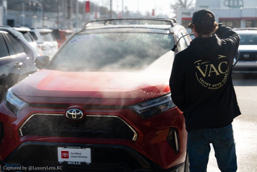 Person spraying water on a red Toyota SUV at a car wash