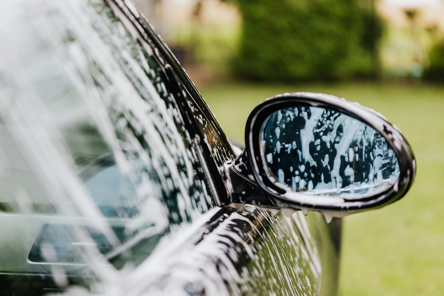 Black car side mirror covered in soapy foam.