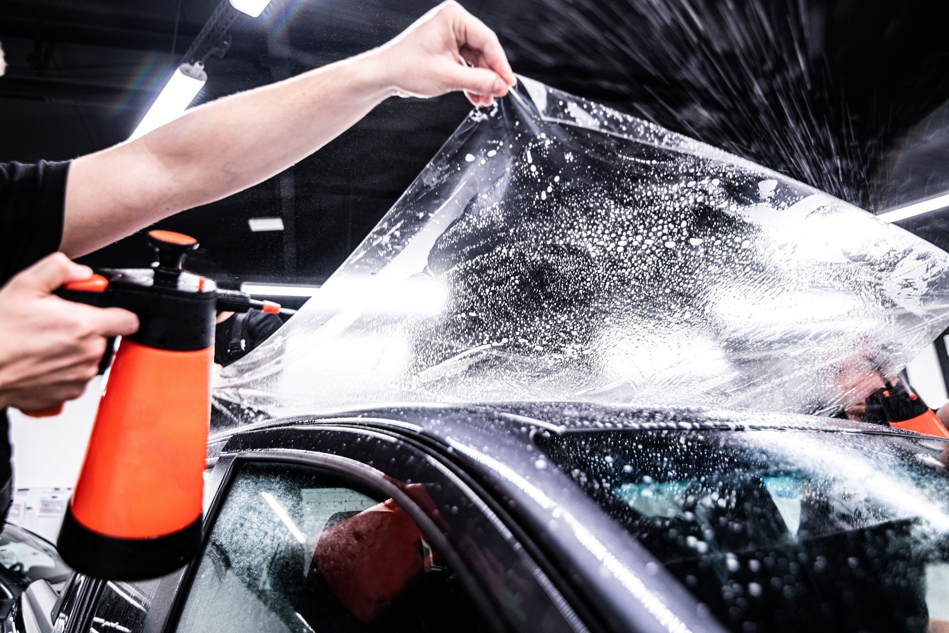 Gloved hand applying a coating to a shiny red car surface.