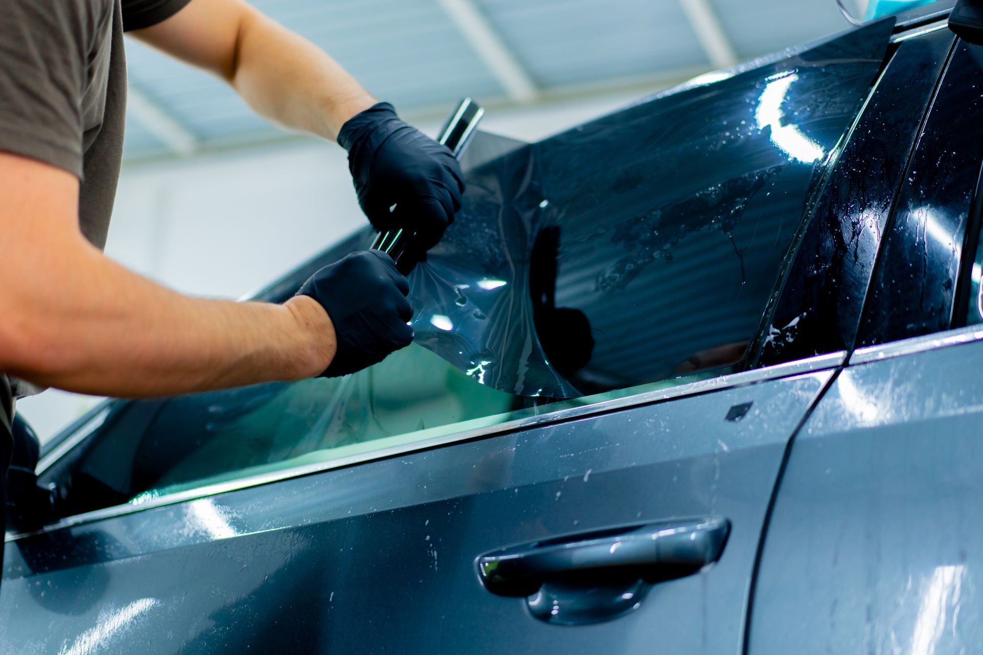 Person in black gloves applying wax to a shiny black car in a garage.