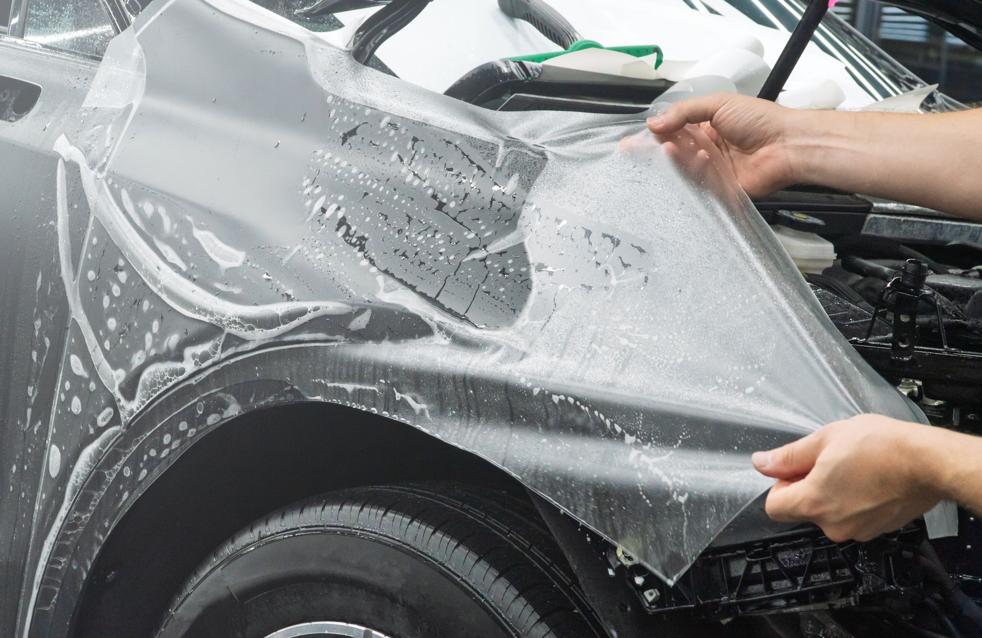 Person in black gloves applying wax to a shiny black car in a garage.