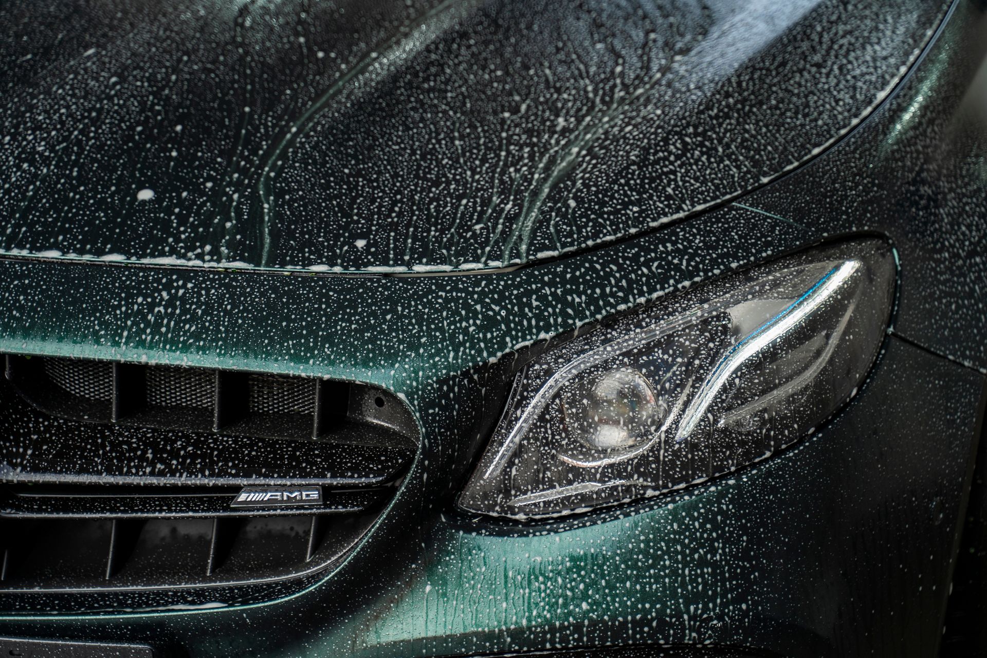 Green car being washed, soapy water on the hood and headlight.
