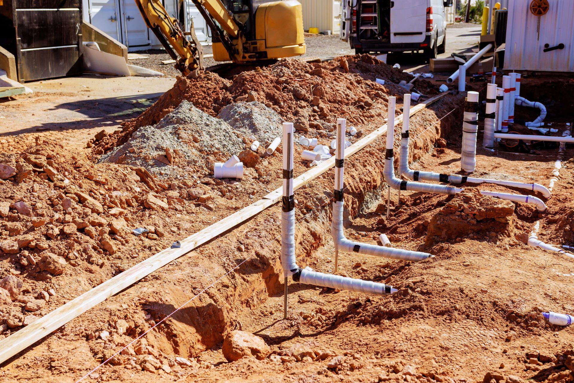 PVC pipes laid in a dirt trench at a construction site, with excavators and dirt piles in the background