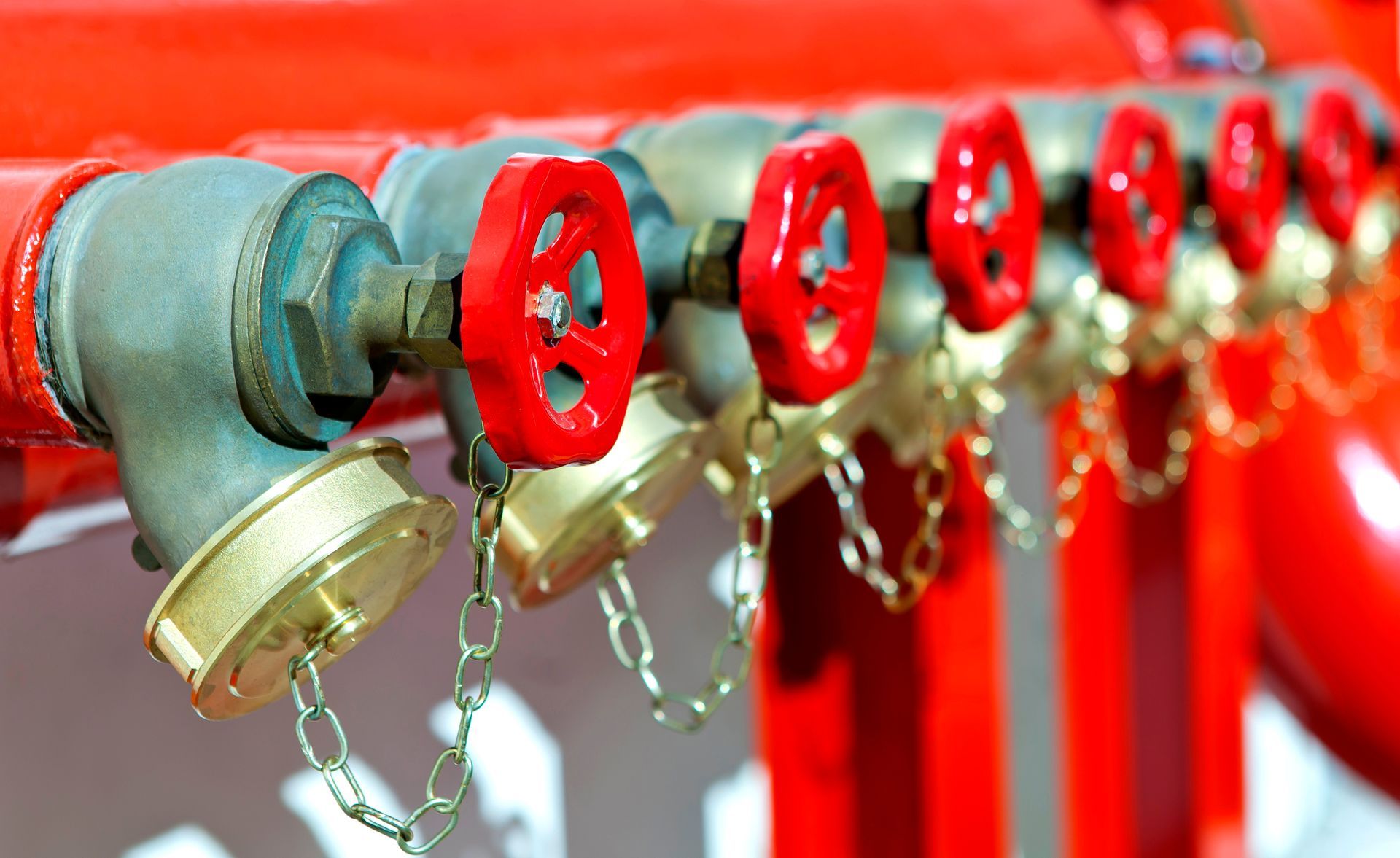 Row of red fire hose valves and brass couplings with hanging chains on a red pipe