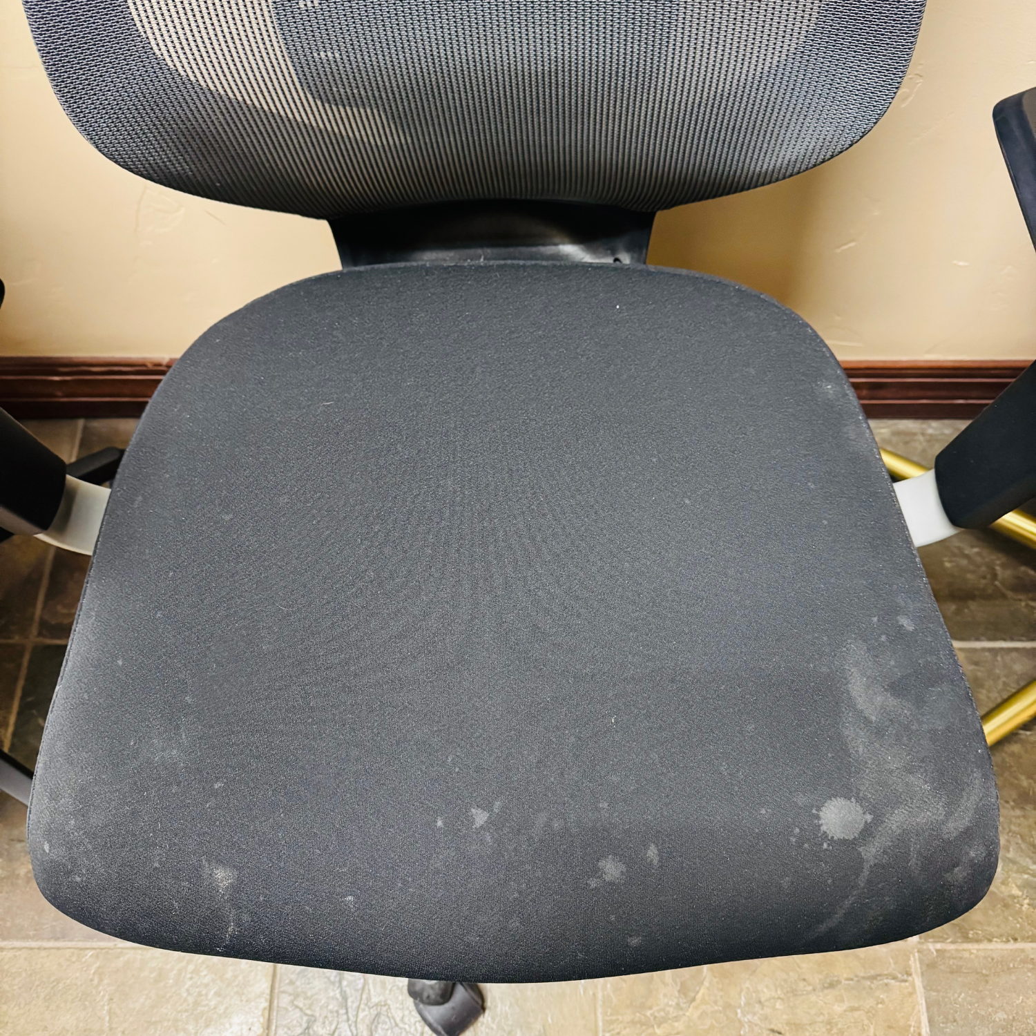 A black office chair with a mesh back and a fabric seat that has visible light-colored stains.
