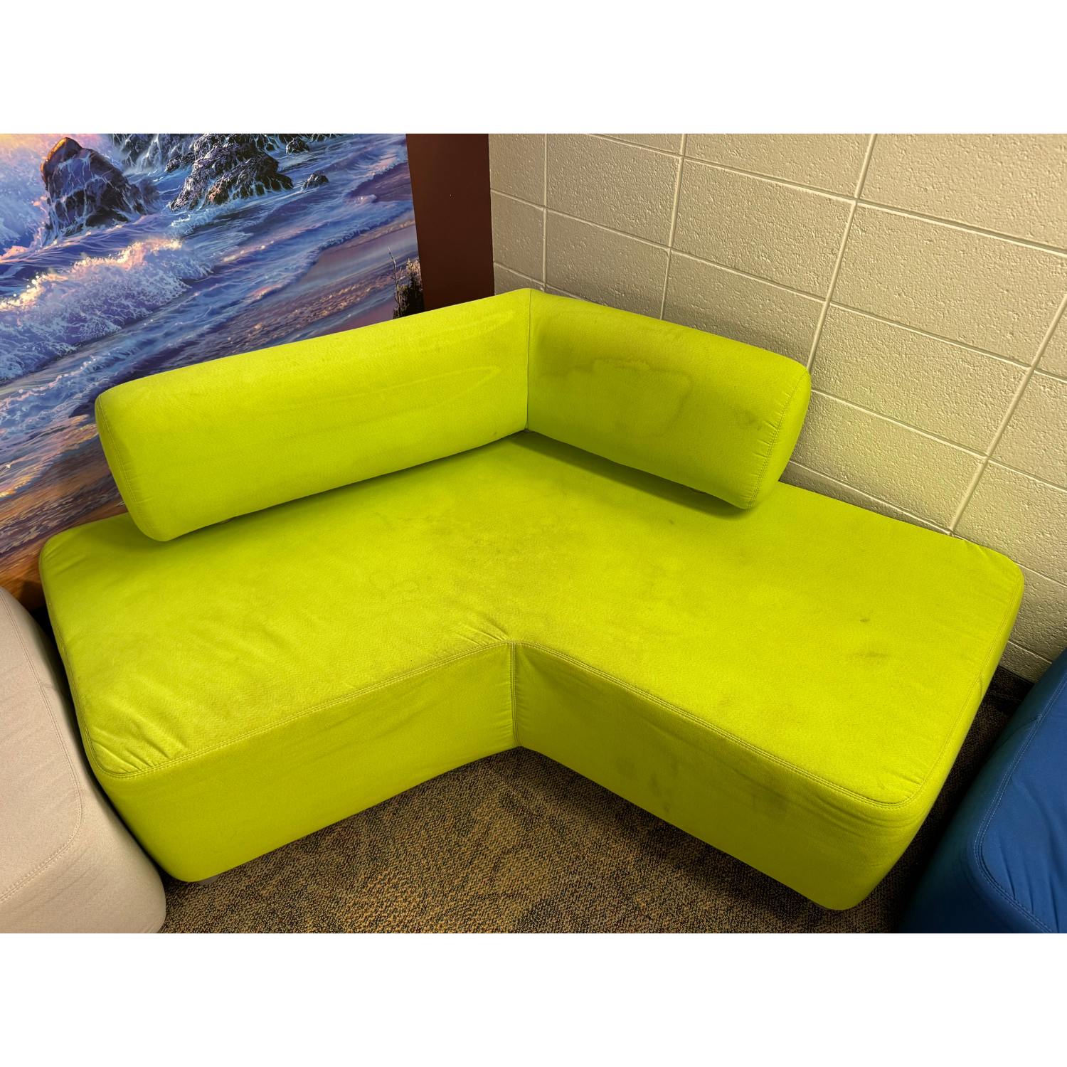 A lime green, L-shaped sectional sofa with a low backrest, positioned in a corner against a textured white wall.