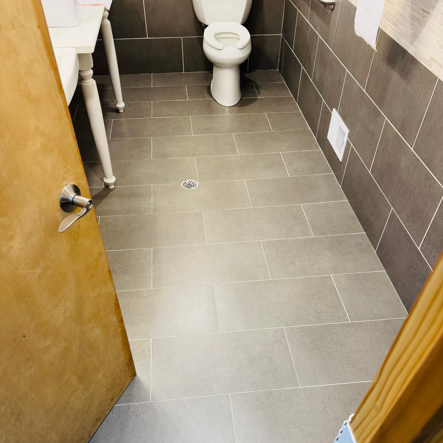 A small bathroom with a beige toilet, gray tiled floor and walls, and a light-colored vanity unit.