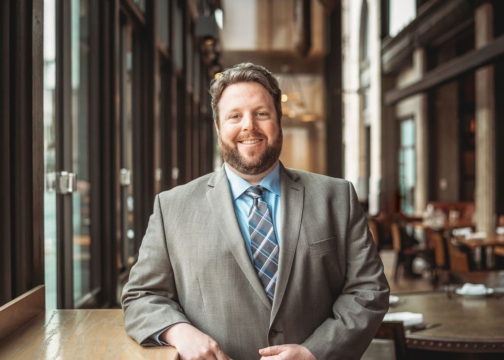 Smiling man in a gray suit and blue tie standing in a modern café corridor