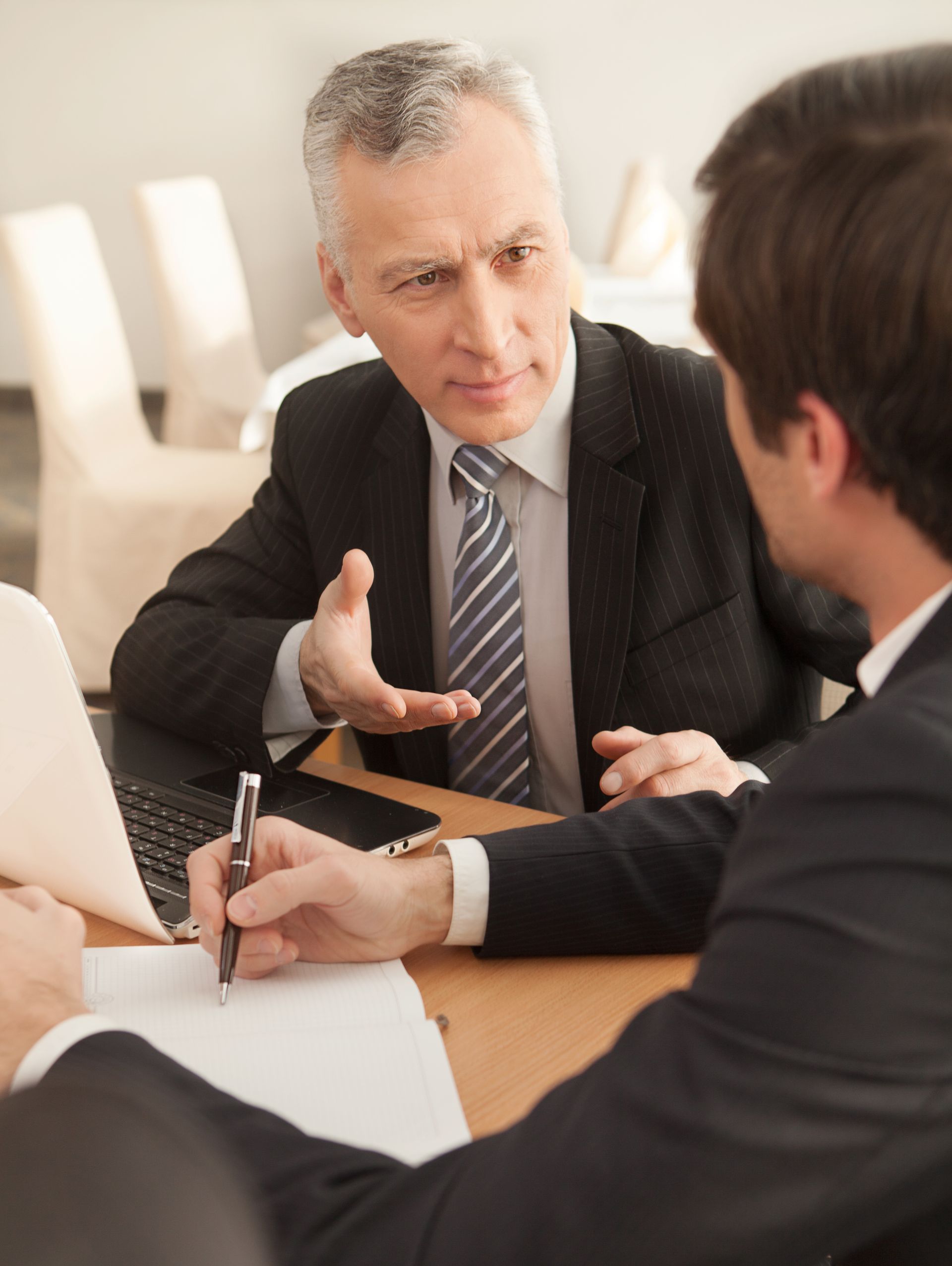 Two people in suits discussing paperwork at a table in a bright office