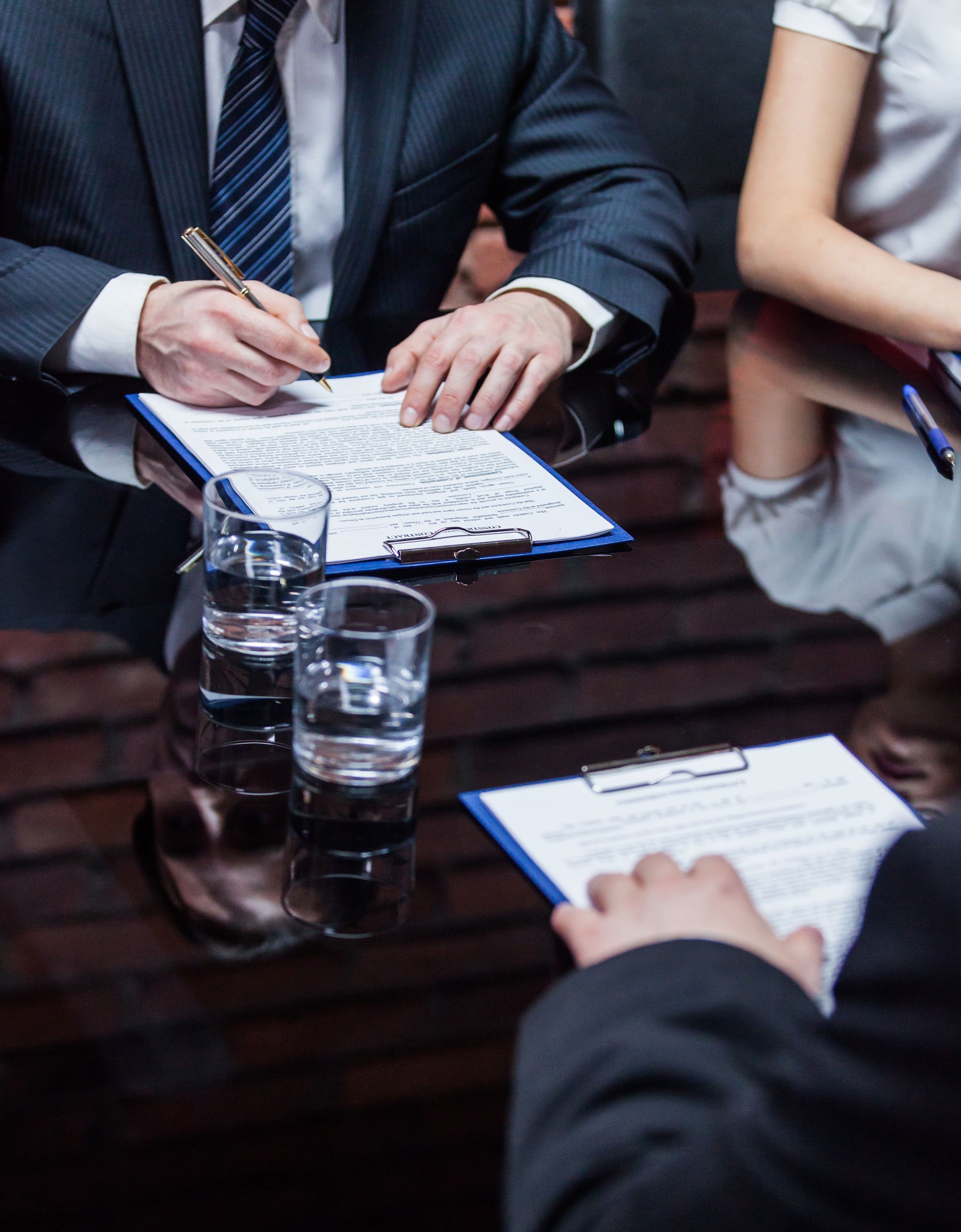 Business meeting with people taking notes around a wooden table with water glasses