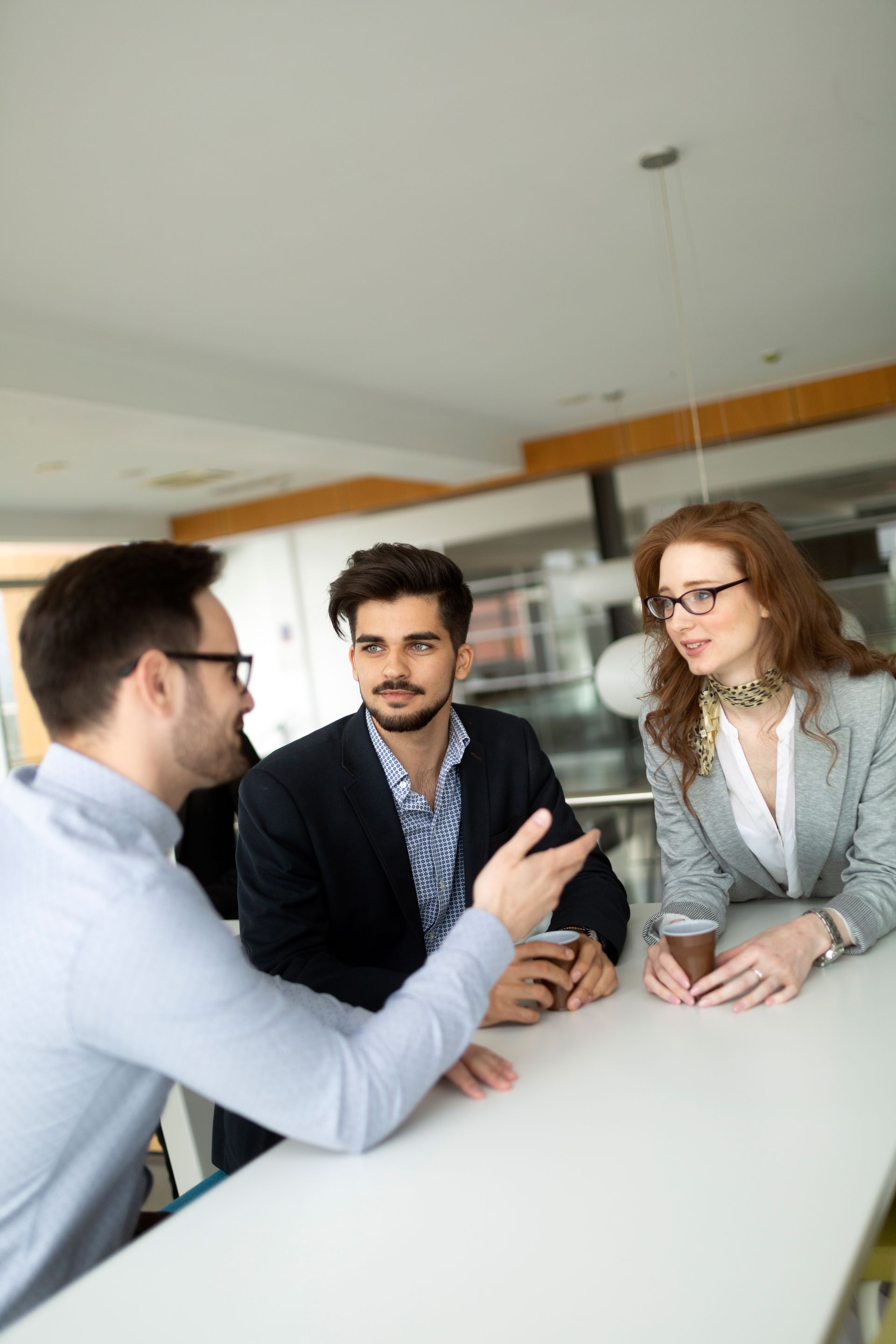 Three colleagues discussing around a white table in a modern office