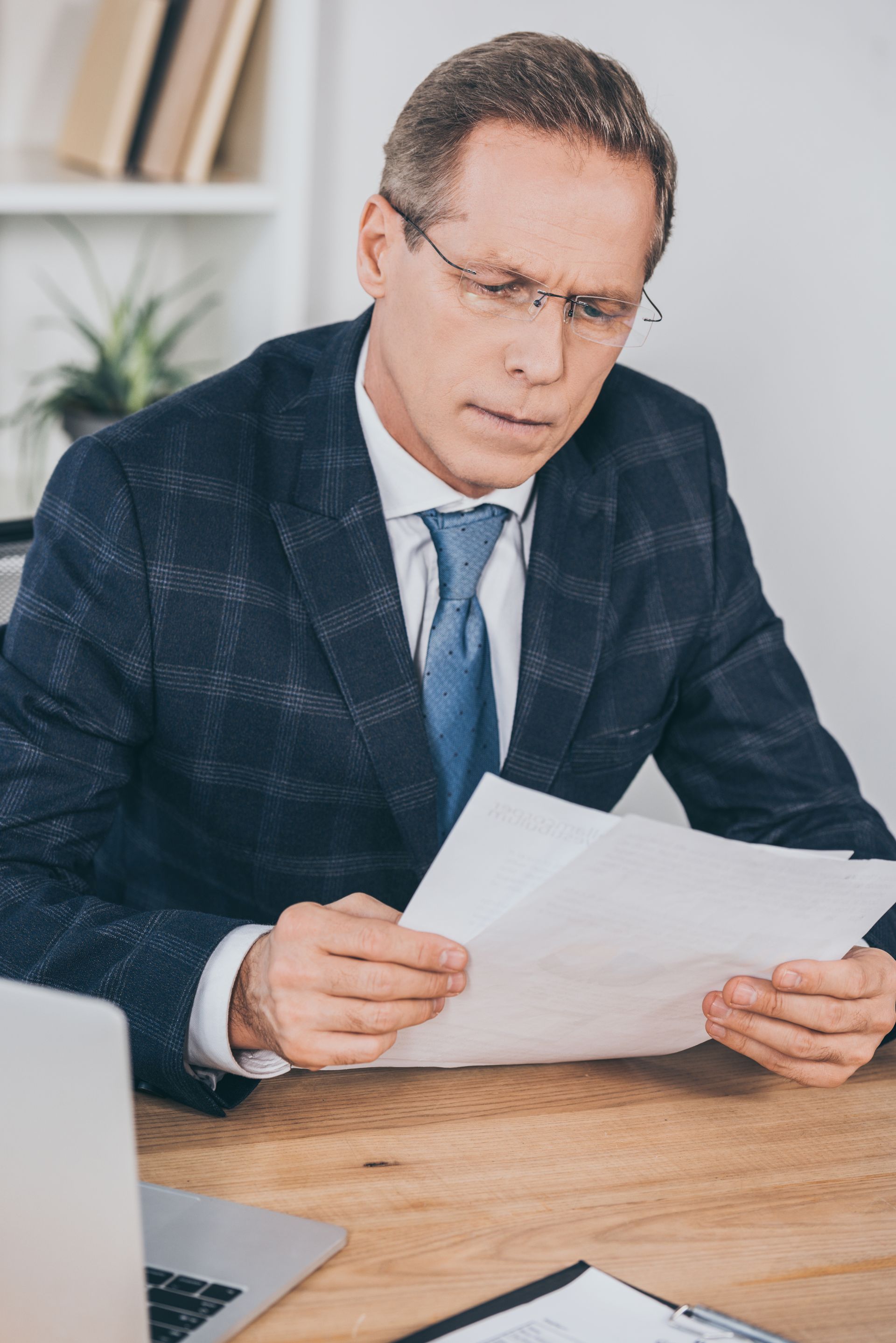 Man in a dark suit reading papers at a desk in an office