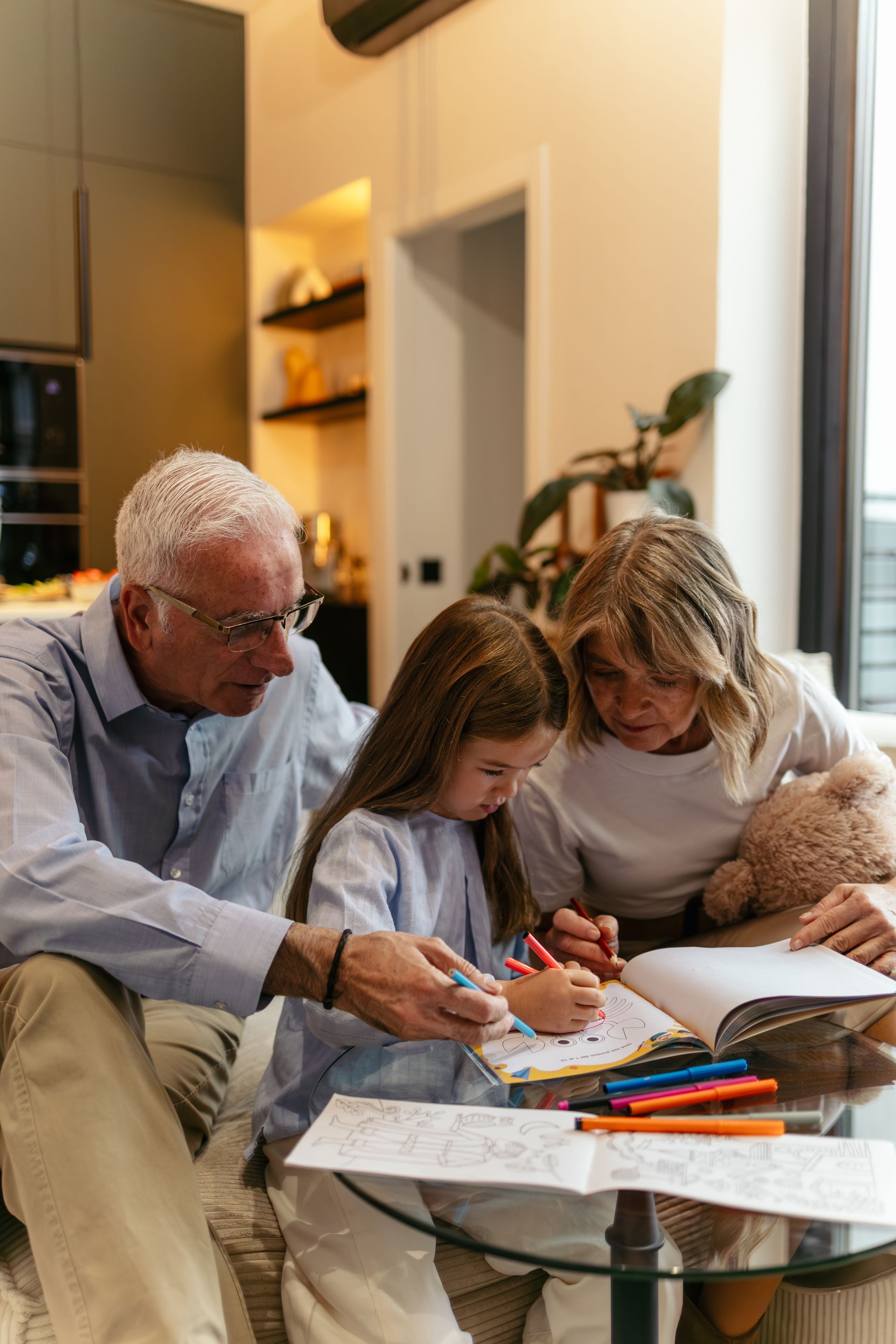 Family sitting on a couch, drawing together at a glass coffee table in a bright living room