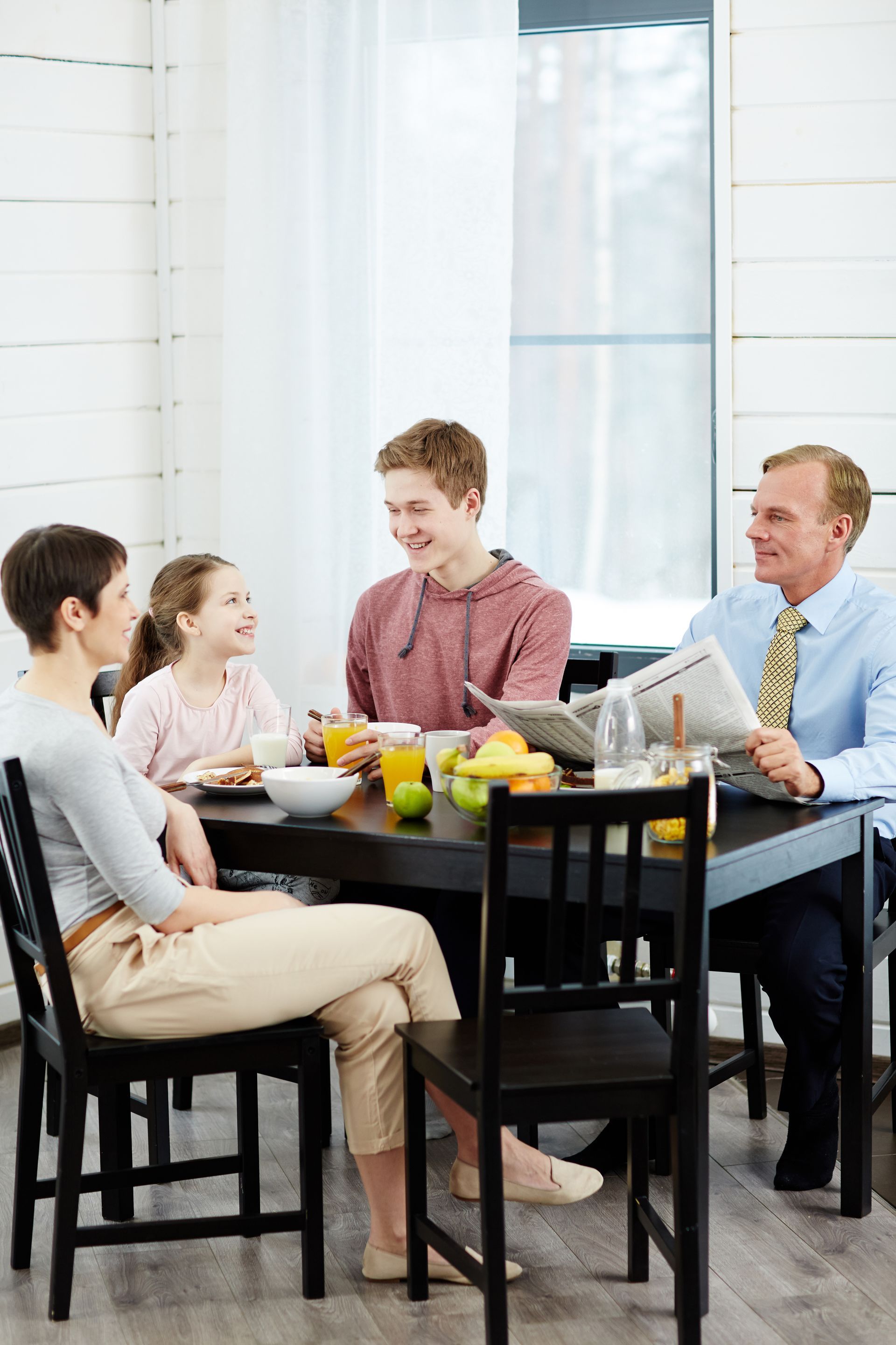 Four people sitting around a table, smiling and eating together in a bright dining room.