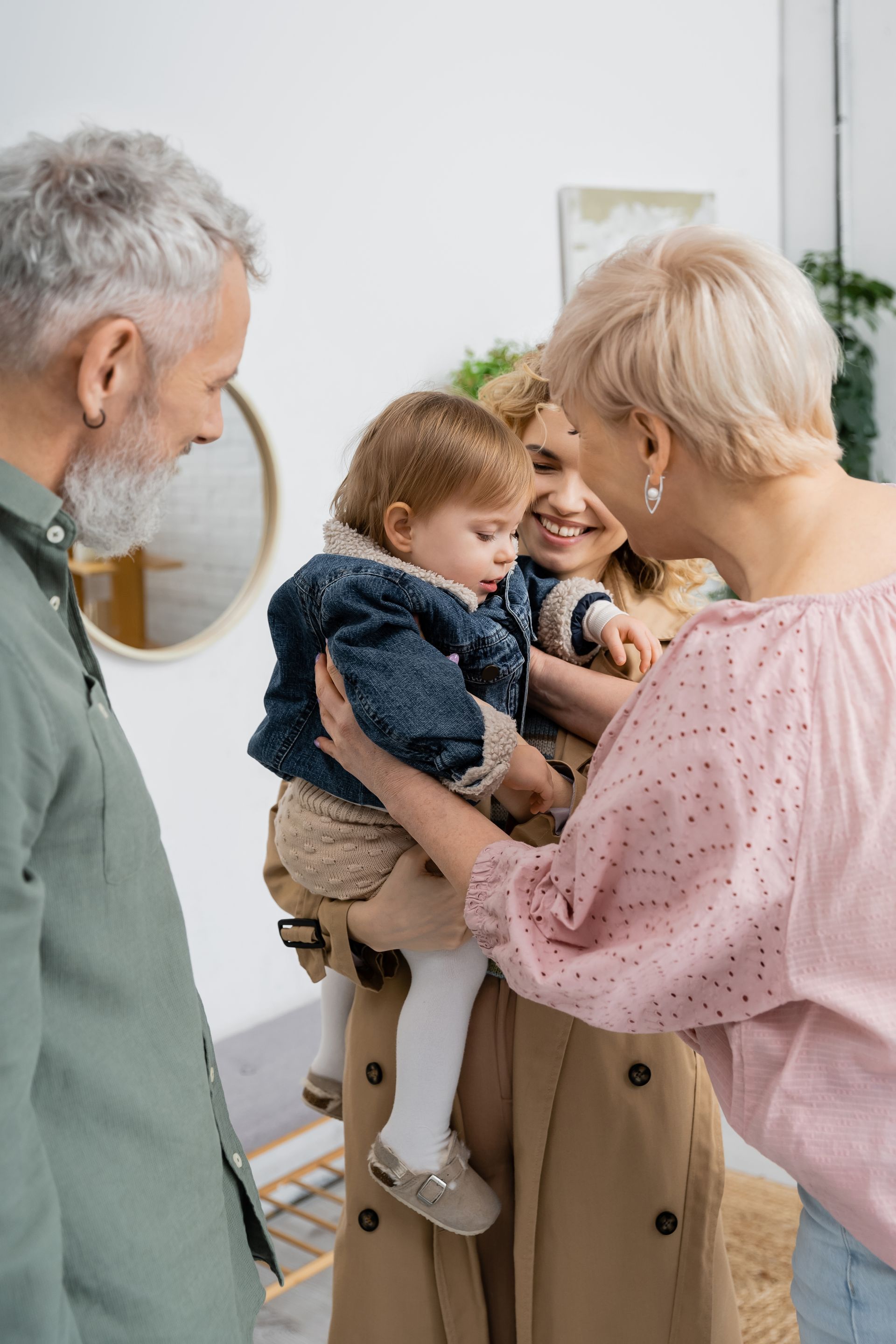 Three adults holding and admiring a smiling toddler indoors.