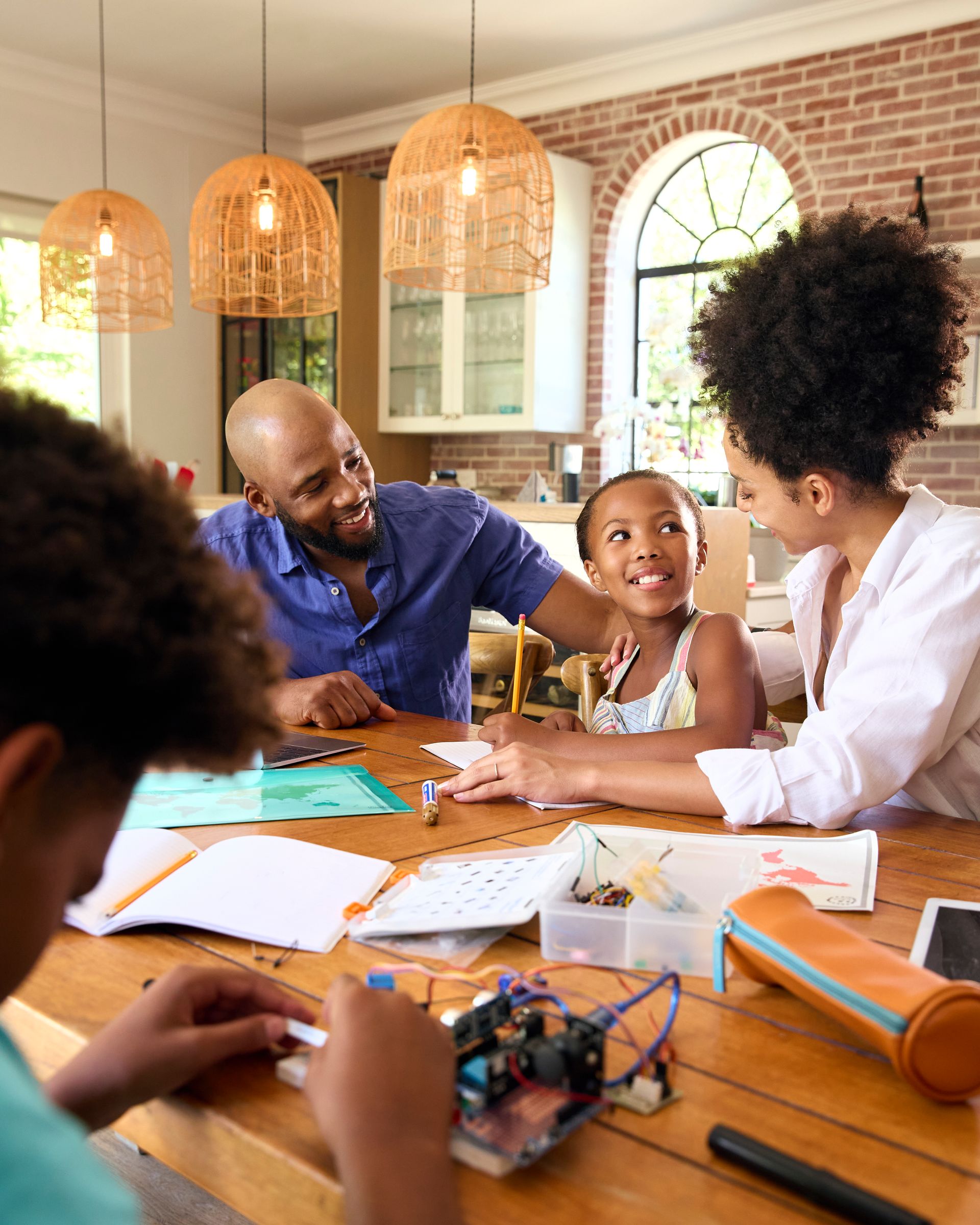 Family gathered around a table, working and talking in a bright brick-walled room