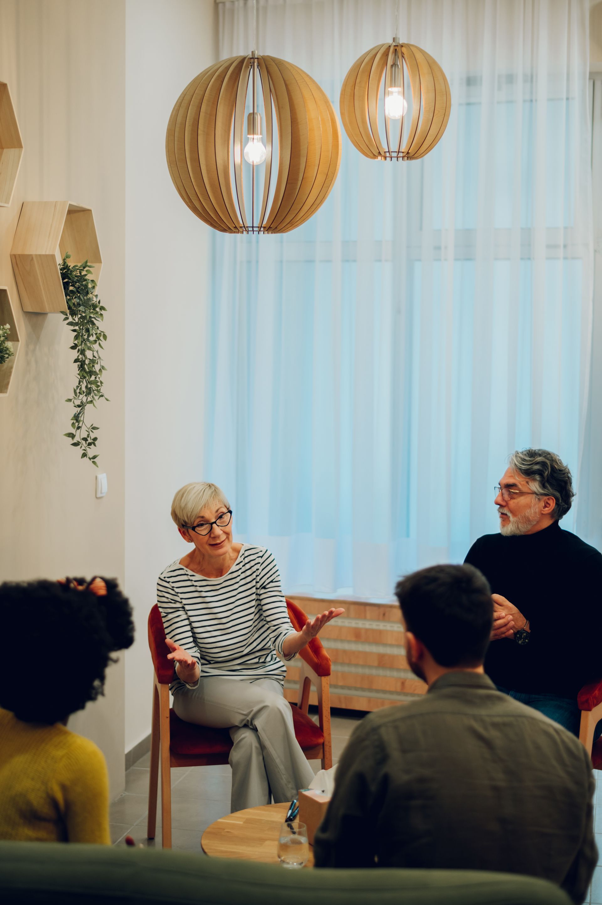 Three people seated in a cozy room, listening during a small group discussion under pendant lights.