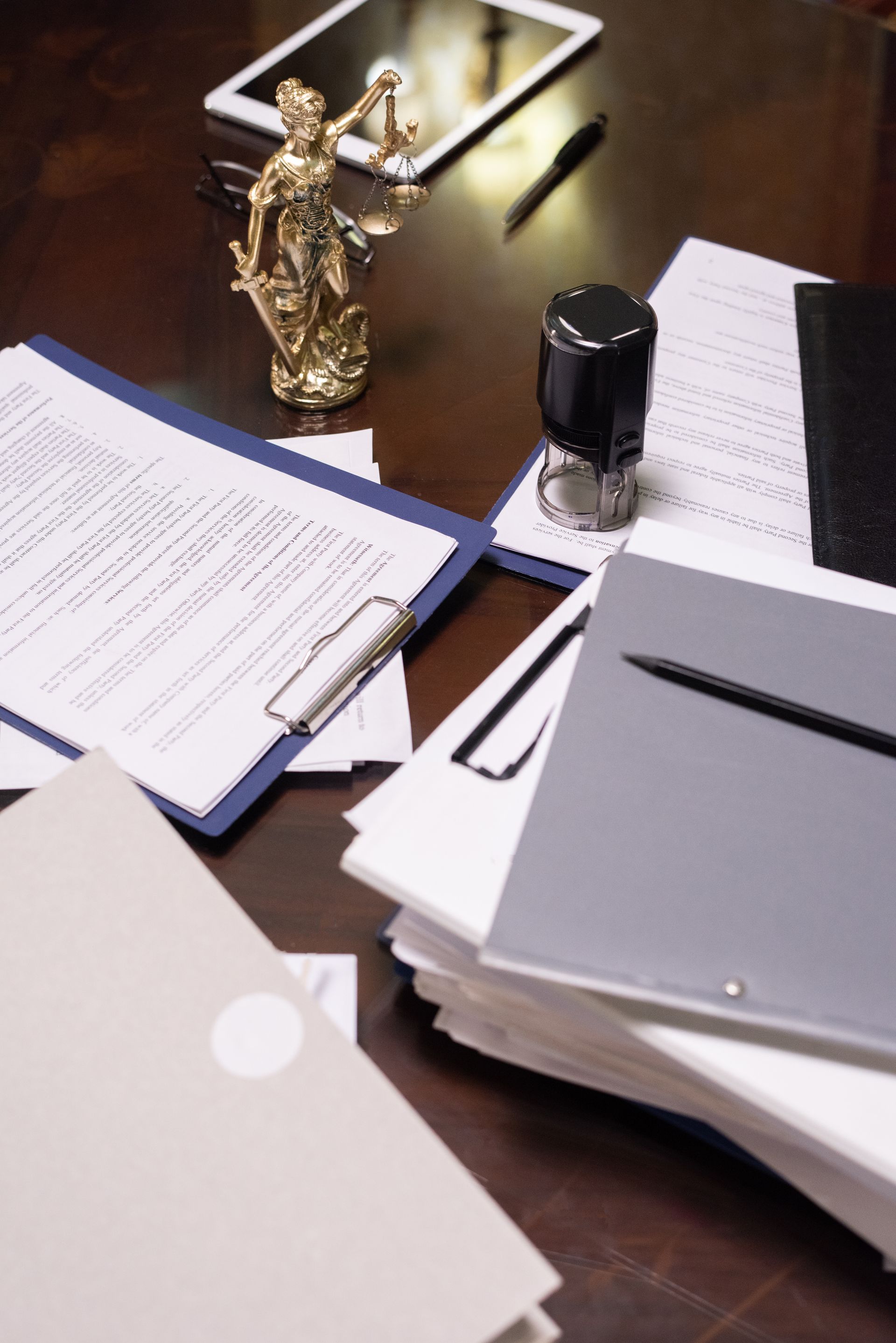 Desk with stacks of documents, a gold figurine, and a pen holder on a dark wood surface.