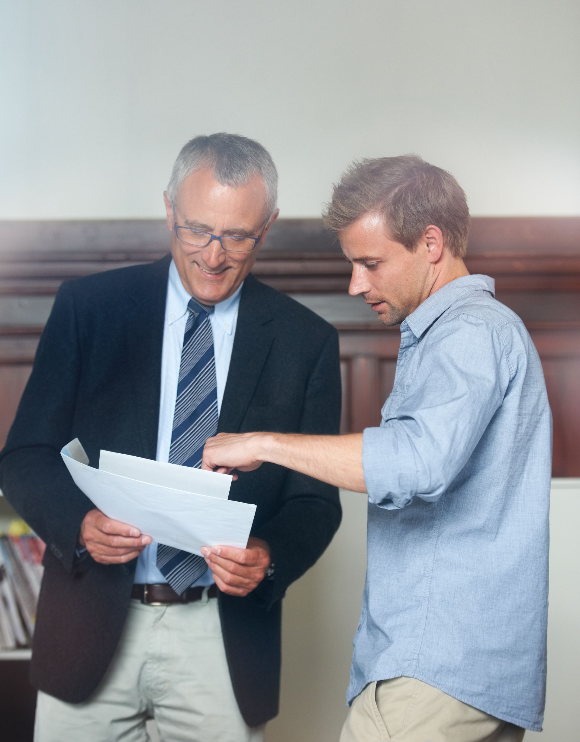 Two men reviewing documents together in an office, one pointing at the papers.