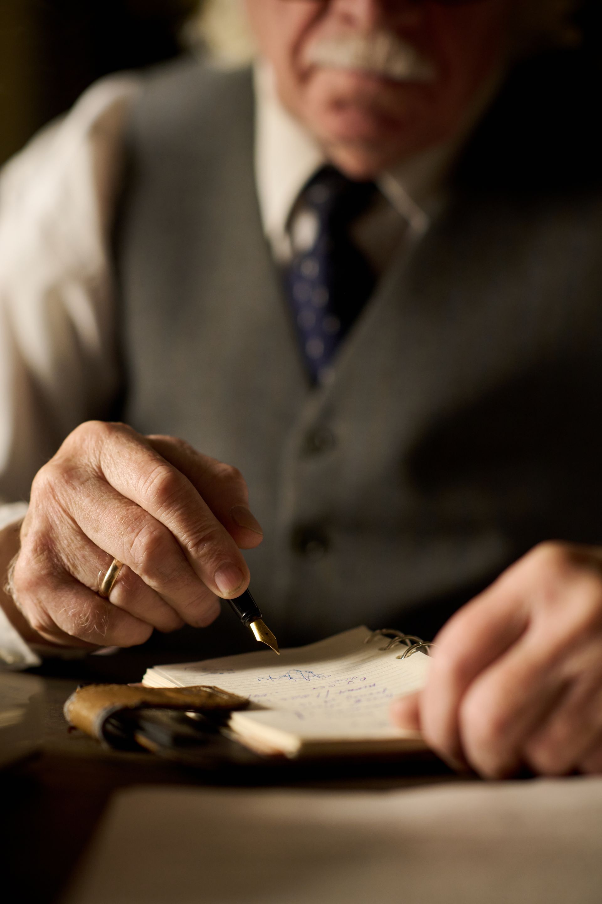 Close-up of a person in a suit signing a document with a pen at a desk