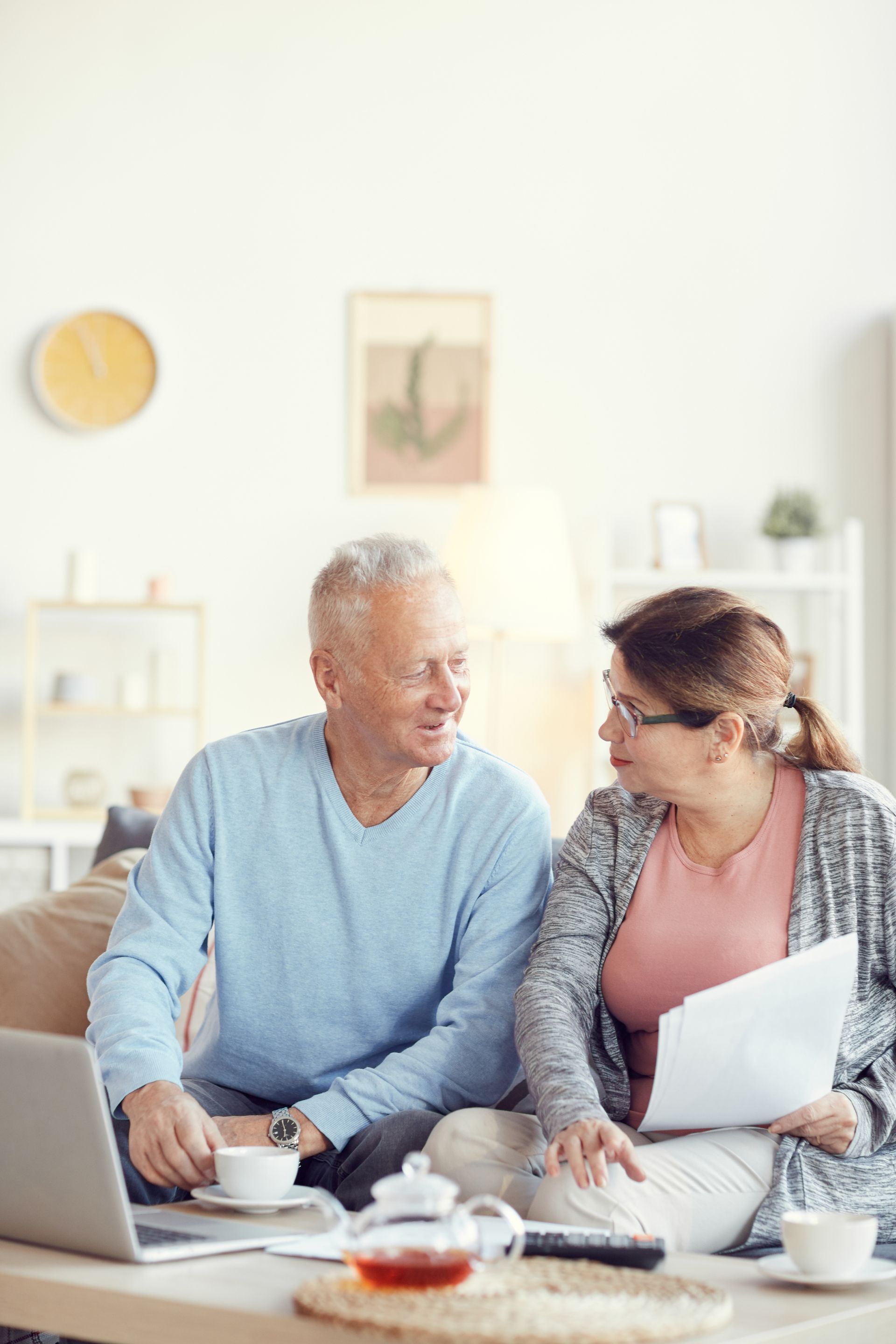 Two people talking at a table with coffee and a laptop in a bright living room