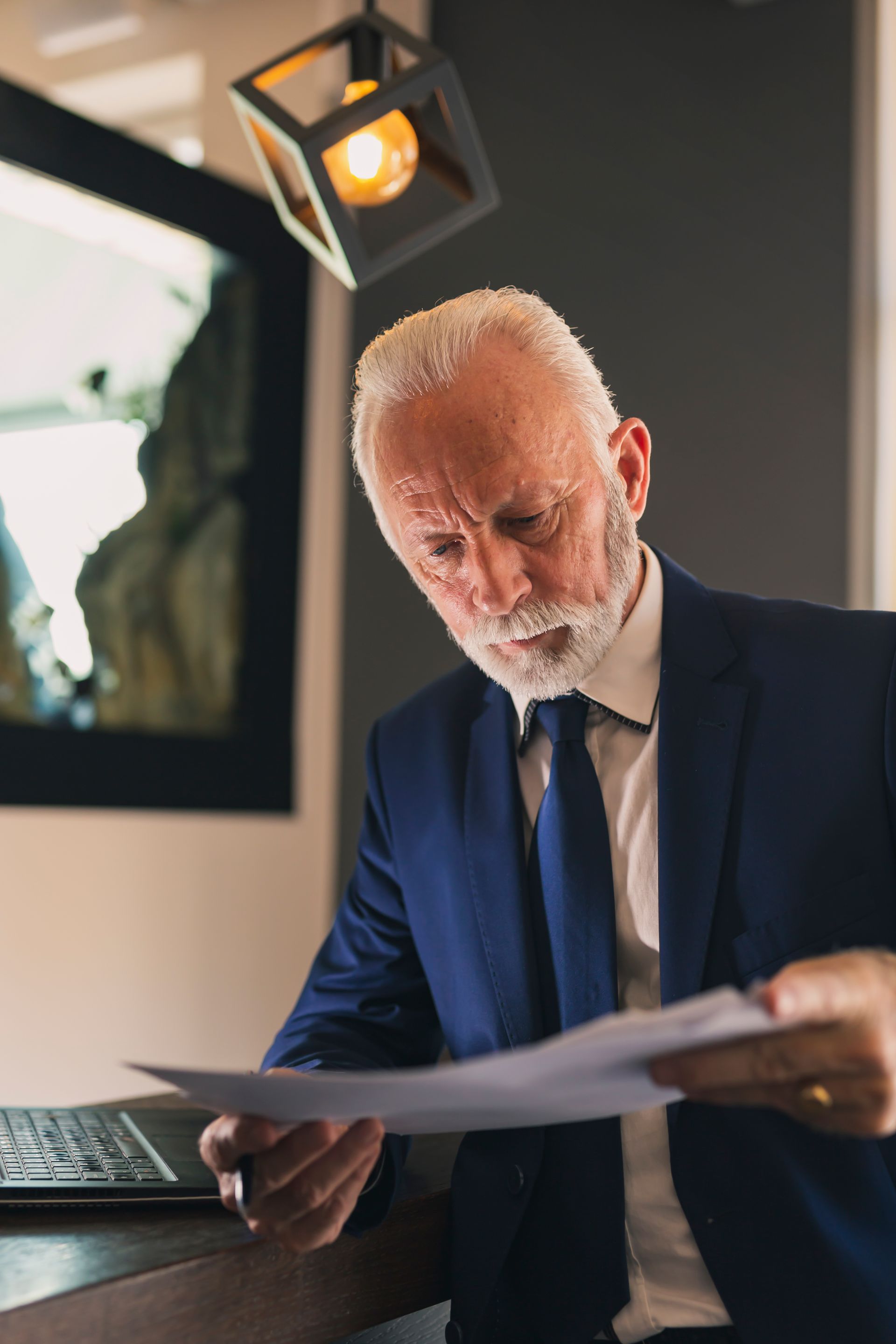 Man in a blue suit reviewing papers at a desk in a warmly lit office
