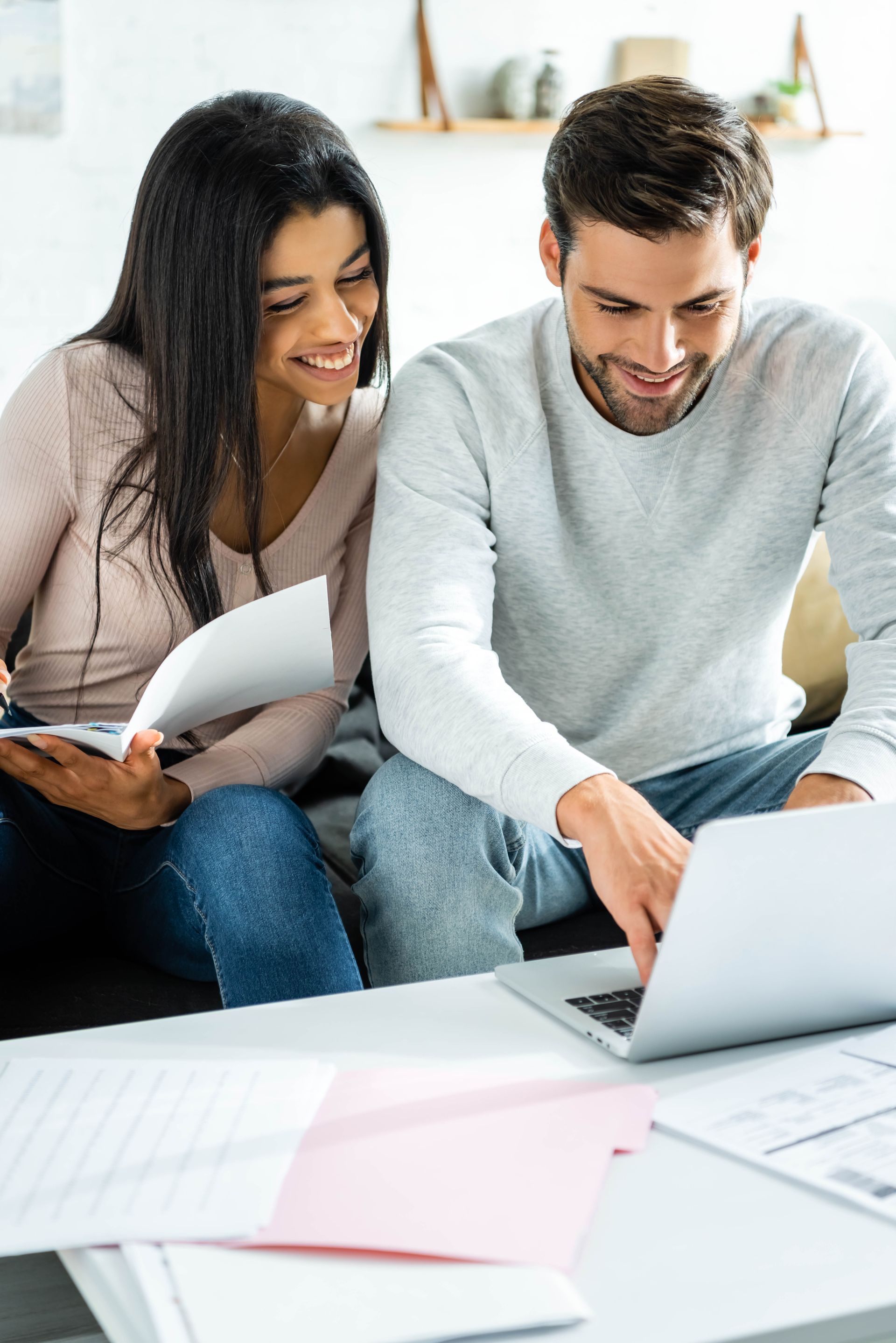 Two people review papers and a laptop at a table in a bright office.