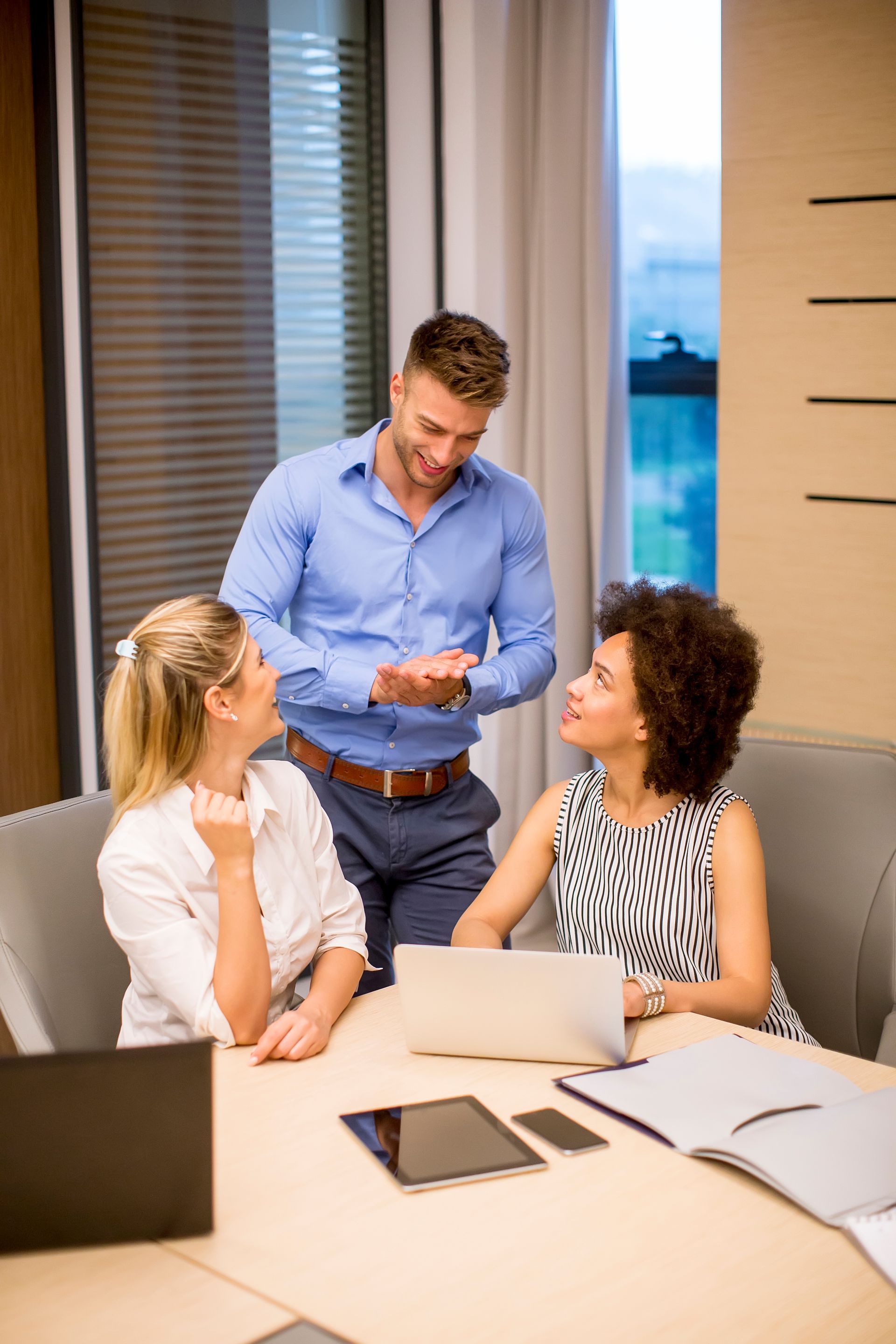 Three coworkers discussing documents around a table in a bright office meeting room.