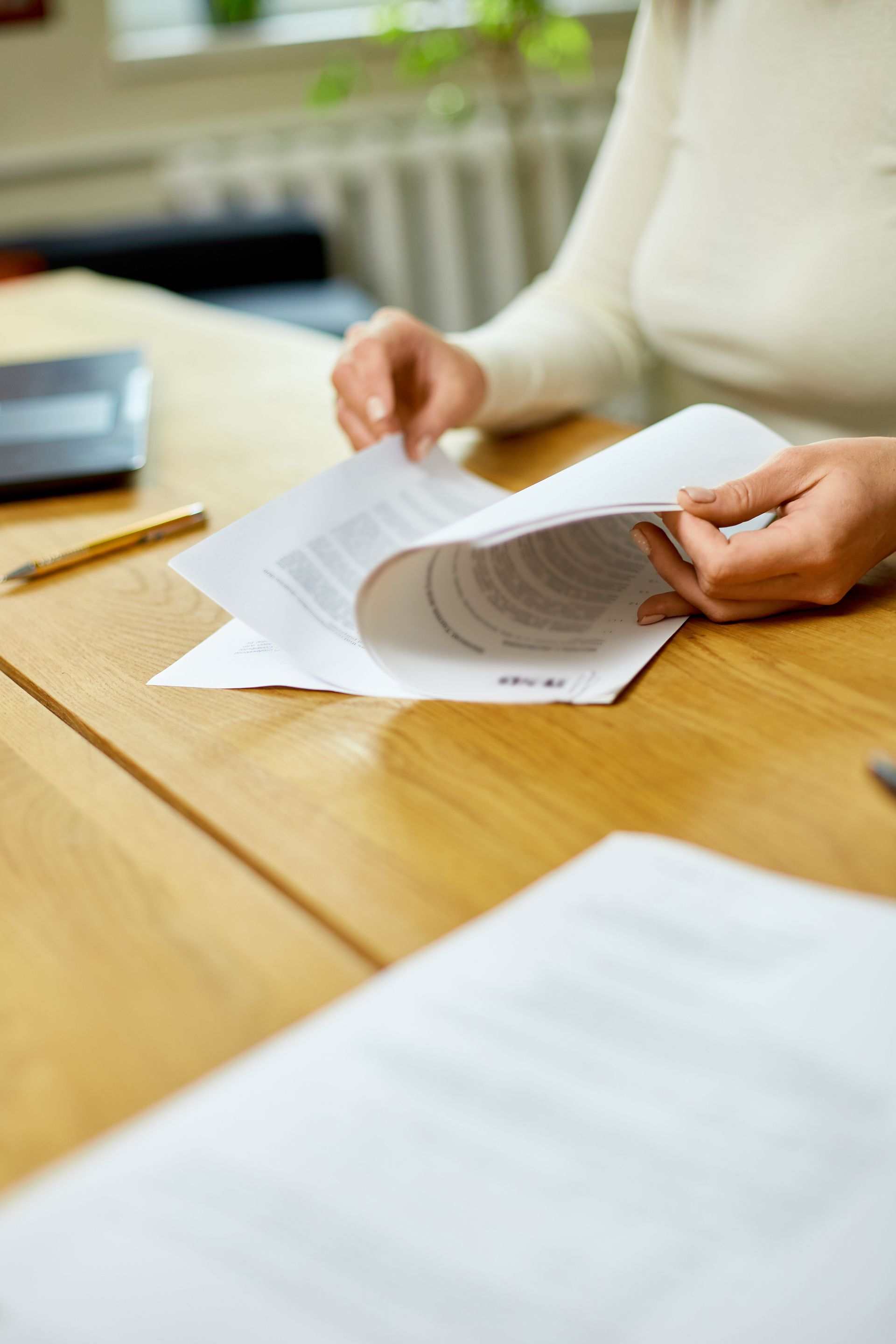 Hands sorting papers on a wooden table in a bright office or home workspace