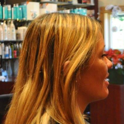 A woman with long blonde hair is smiling in a salon