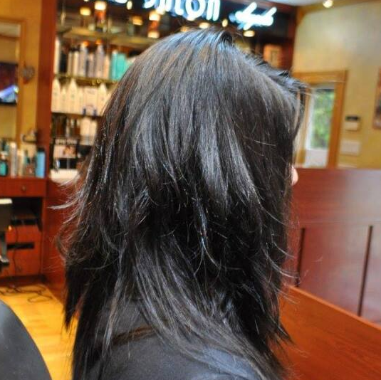 A woman with long black hair is standing in front of a salon sign