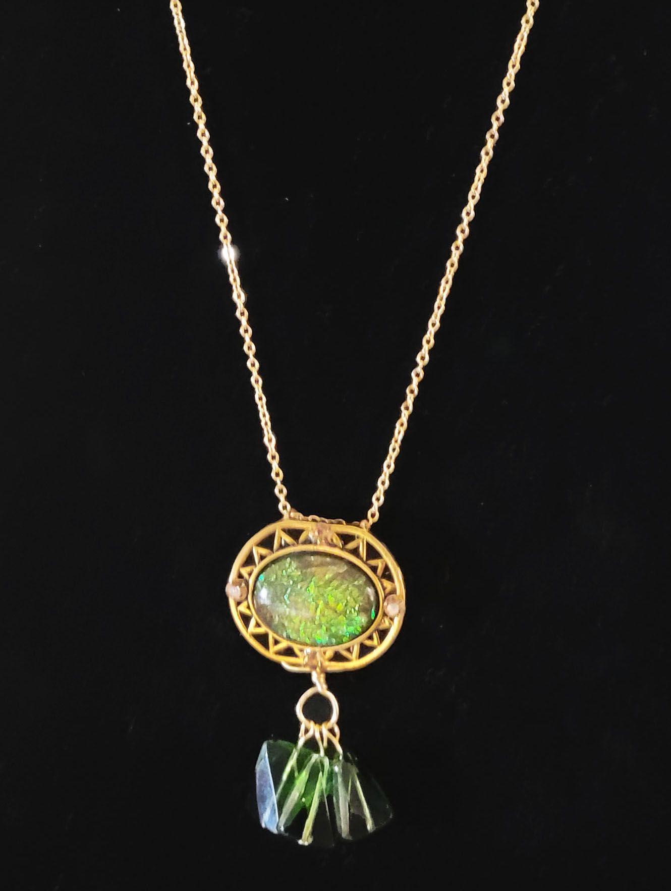 A gold necklace with a green pendant on a black background