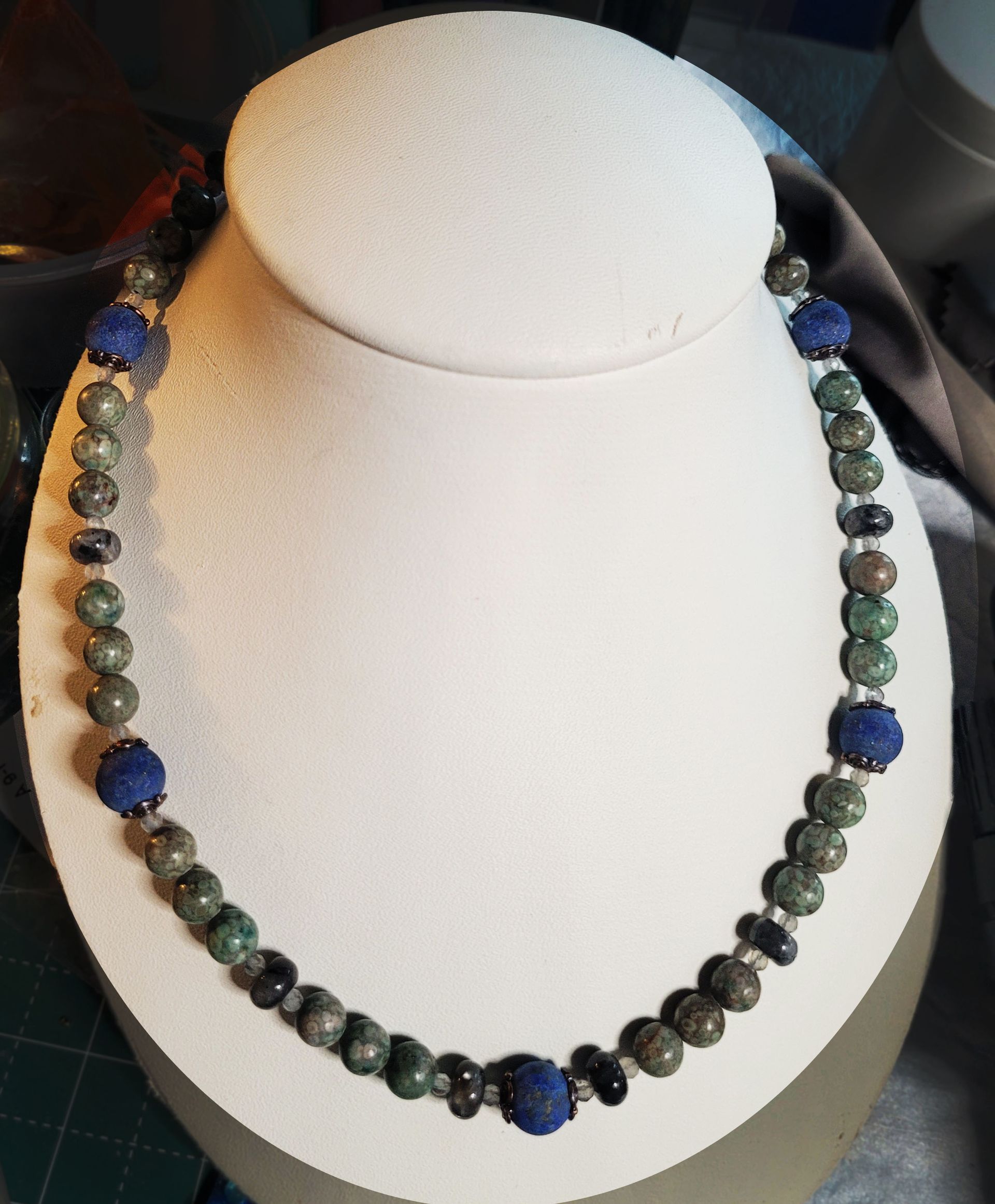 A necklace with blue and green beads is on a mannequin