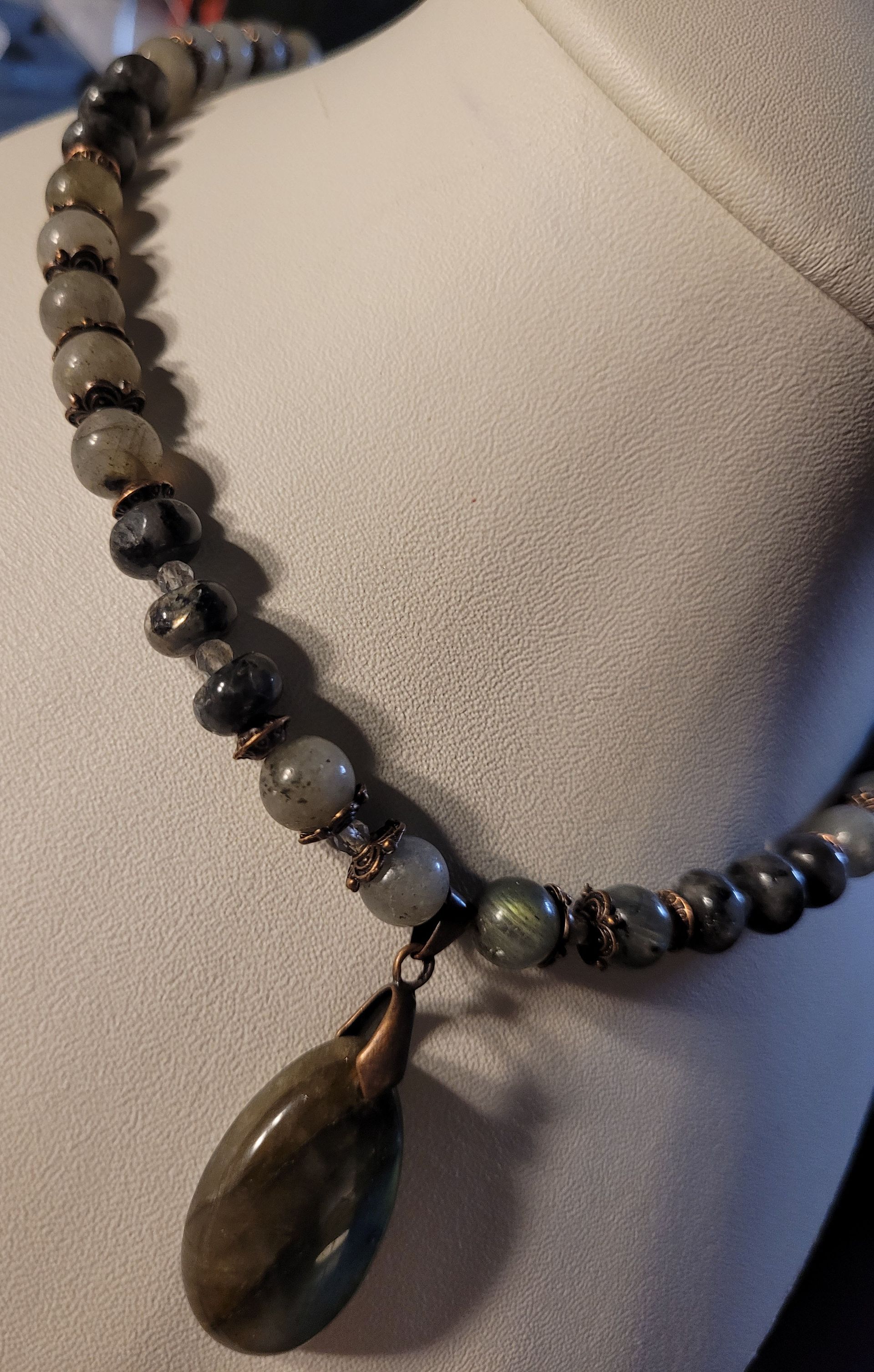 A close up of a necklace with beads and a pendant on a mannequin.