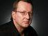 A man wearing glasses and a black shirt looks at the camera
