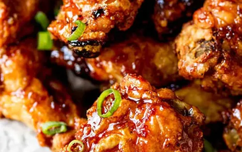 Close-up of crispy glazed chicken wings with green onion garnish.