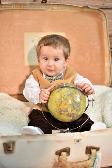 Un niño sentado en una maleta abierta, sosteniendo un globo terráqueo, con expresión neutra.