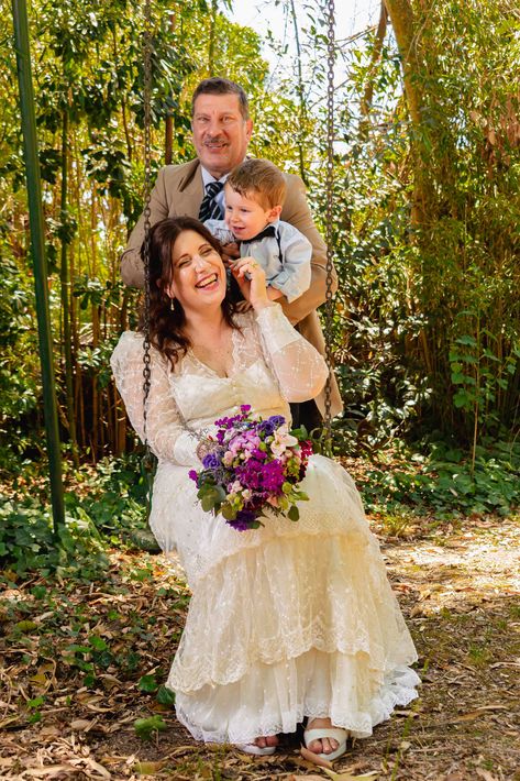 Retrato familiar al aire libre con una novia sosteniendo flores, un hombre de pie detrás de ella y un niño sobre sus hombros.
