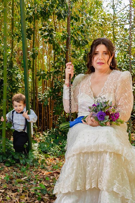 Una mujer con un vestido color crema está sentada en un columpio sosteniendo flores, con un niño de pie .