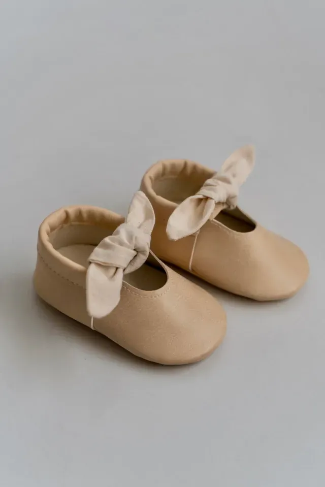 Zapatos de bebé color beige con inserciones decorativas extraíbles en blanco y marrón sobre fondo blanco.