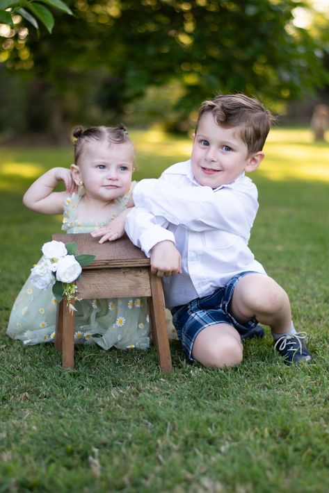 Dos niños sentados en el césped junto a un pequeño taburete de madera en un parque soleado.