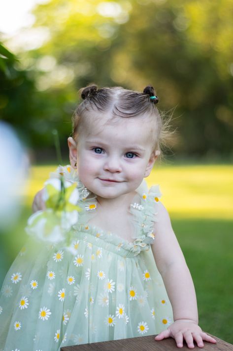 Niña pequeña con un vestido verde claro de pie al aire libre en un jardín soleado.