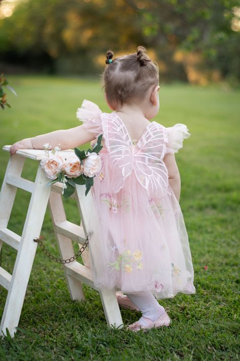 Una niña pequeña con un vestido rosa apoyada en una valla blanca en un jardín cubierto de césped.