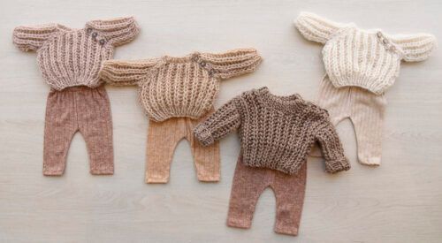 Cuatro suéteres y pantalones de bebé tejidos a mano en color beige, marrón y blanco, extendidos sobre una superficie clara.