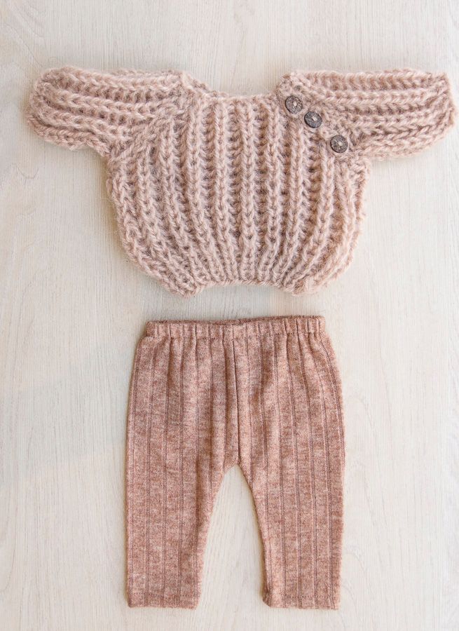 Cuatro suéteres y pantalones de bebé tejidos a mano en color beige, marrón y blanco, extendidos sobre una superficie clara.