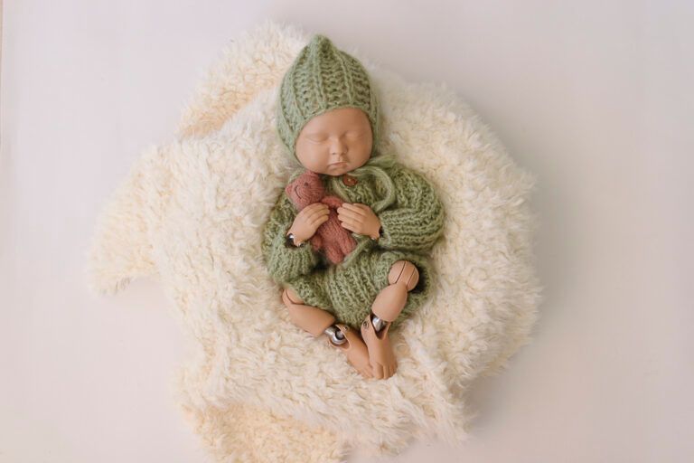 Pelele de bebé de punto verde y gorro con orejas de conejo sobre fondo blanco con una pequeña.