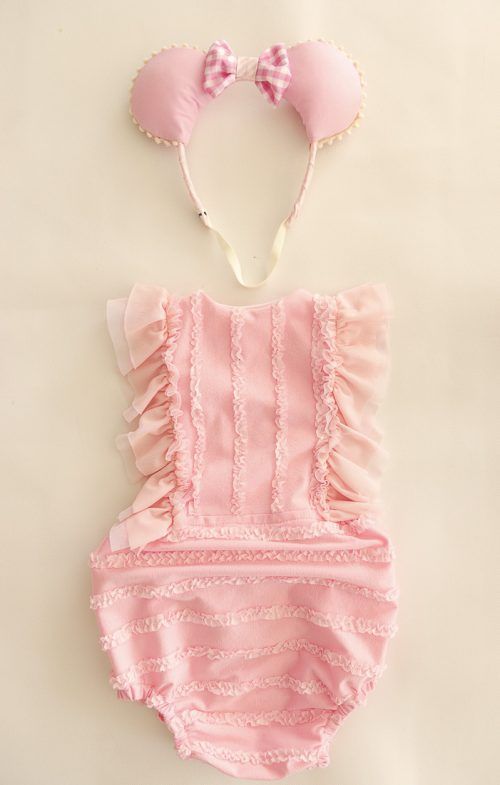 Traje de baño rosa para bebé con gorro a juego, extendido sobre un fondo beige.